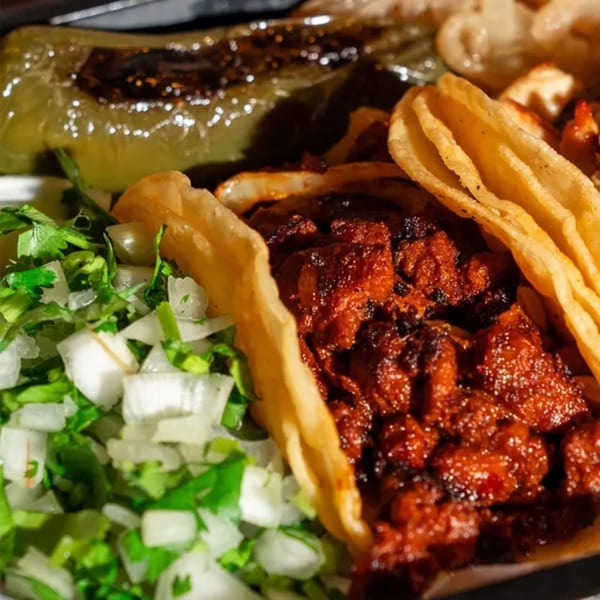 Close-up of El Paisa Cocina Mexicana's tacos with red meat, cilantro, onions, and a roasted pepper.