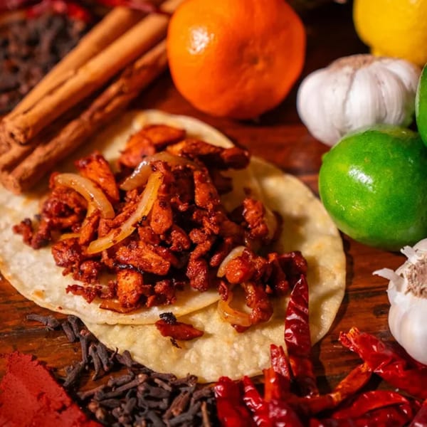 El Paisa Cocina Mexicana taco with meat and onions, surrounded by spices, limes, and garlic.