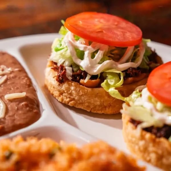 Mexican sopes topped with meat, lettuce, sour cream, and tomato, served with refried beans and rice.