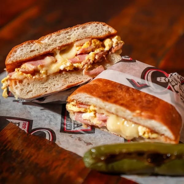 Two halves of a Mexican torta sandwich with ham, scrambled eggs, and melted cheese.